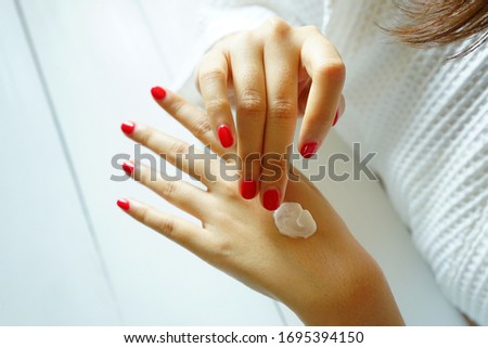 Beauty and body care theme young woman in white bathrobe applying cream on her backhanded. Beautiful female hand and fingers with red nail polish taking care of her dry skin by applying cream.