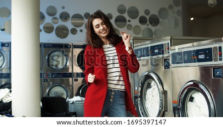 Caucasian joyful pretty and stylish woman having fun and dancing in laundry service room while machines washing working in public laundromat.  Royalty-Free Stock Photo #1695397147