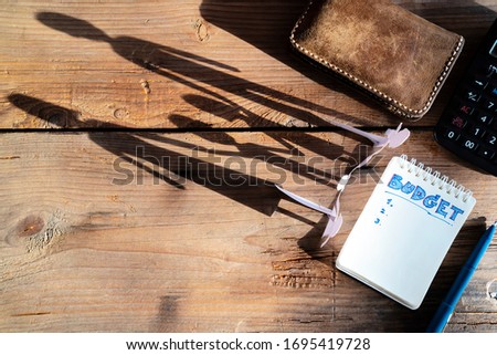 The family of paper cut placed on a wooden table. There is a shadow of a family holding hands, Budget planing concept. Top view of notepad with word Budget, Copy space