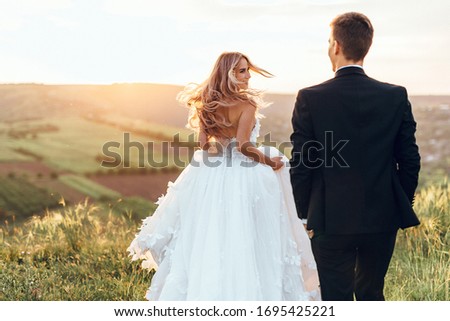 Happy young bride woman in white dress running in the sunset light with blowned hair. Back view. Royalty-Free Stock Photo #1695425221