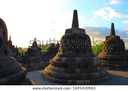 Borobudur temple in Jogjakarta Indonesia. Central Java. Picture of the temple Borobudur at sunset with blue sky and green trees. Multiple stupa's shown in foreground of photo. Stupa's at sunset. 