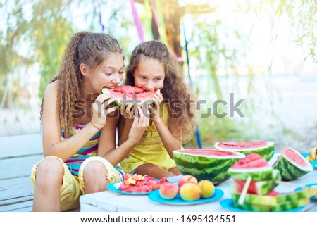 Cheerful friends on a picnic eating watermelon on a sunny day. Having fun together.  Concept summer time, friendship, childhood Fruit canapes, peach, lices of watermelon  lie on the table