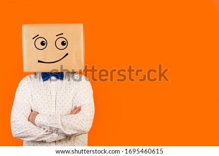 Man standing with his head in a box and suspicious gesture drawn on it and on a orange background. Front view. Copy space Royalty-Free Stock Photo #1695460615