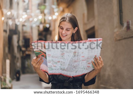 Girl is smiling and deciding what restaurant to visit in the evening, she found out an article in the guide providing the information about outdoor activities and compose a program of her travel. Royalty-Free Stock Photo #1695466348