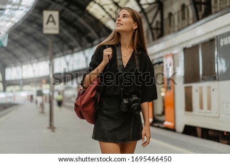 Tourist takes all needed equipment for the trip, she takes the camera for memorizing the main events of her travel. Girl goes out of the railway station and observe buses timetable.

