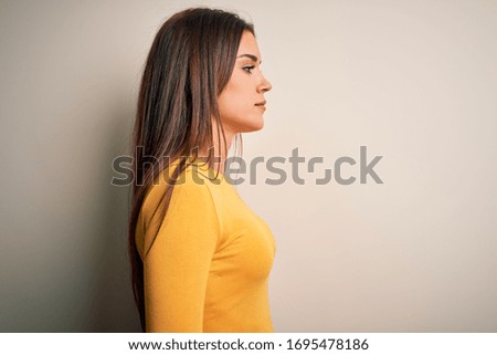 Young beautiful brunette woman wearing yellow casual t-shirt over white background looking to side, relax profile pose with natural face with confident smile.