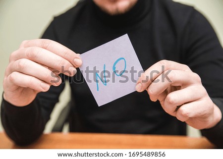 A man holding piece of paper showing word "No"
