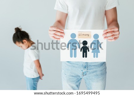 selective focus of father holding paper with drawn family and alimony lettering near upset african american daughter isolated on white