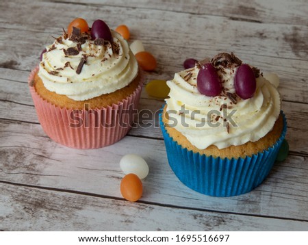 Colorful cupcakes decorated with creamy frosting jelly beans and chocolate sprinkles on wooden surface