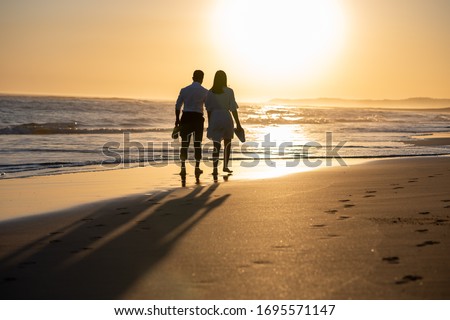 Couple walking along coastline during sunset Royalty-Free Stock Photo #1695571147