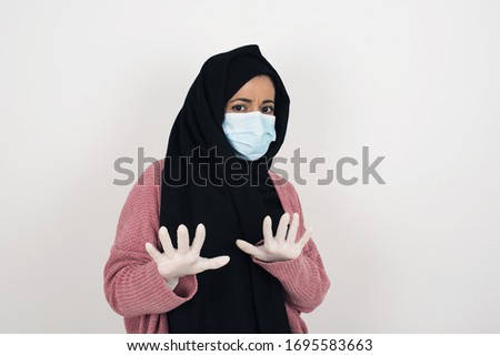 Beautiful Muslim  girl over isolated background afraid and terrified with fear, and disgusted expression stop gesture with both hands saying: Stay there. Panic concept
