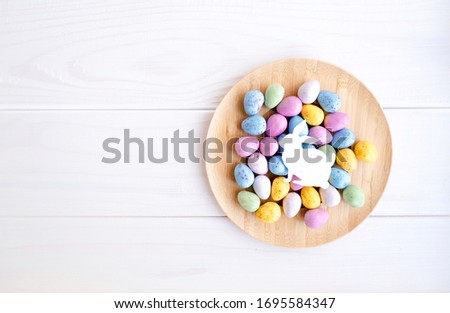 Easter background with colorful eggs and paper bunny silhouette on wooden plate. White wooden rustic background. Happy Easter. Space for text. Place for text