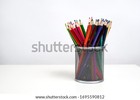 Various color pencils in silver office cup on white table and white background. School. Kids.