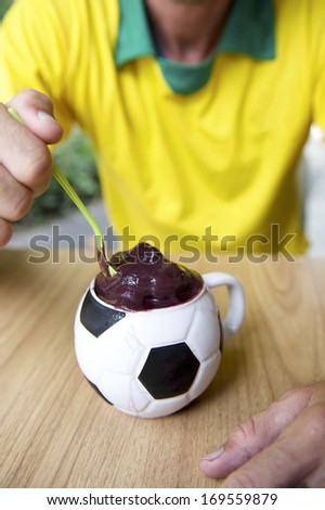 Brazilian soccer player sits eating acai from a football cup