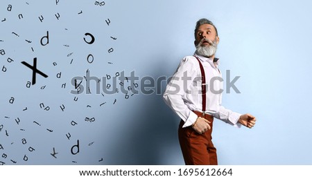 elderly male in white shirt, brown pants and suspenders, bracelet. He running from black letters randomly located on left side of photo, blue studio background. Close up, copy space