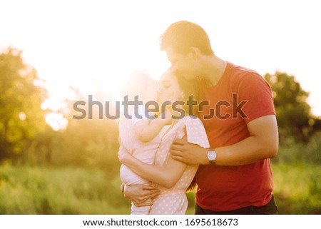 Happy young family walking in the park at sunset. Mom, dad and little daughter having fun in summer park. The concept of a happy family. Parents hold the baby's hands. Kisses and hugs.
