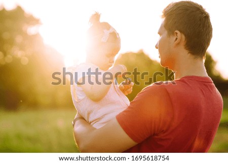 Happy dad and little baby girl  having fun in summer park at sunset. Dad plays with small child on sunny field. Kisses and hugs of father and daughter. Family  and fatherhood concept.