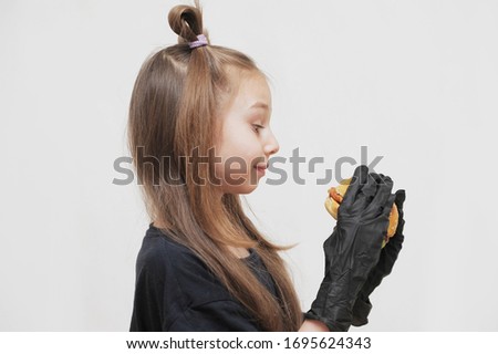 Cute caucasian little girl with black gloves eats hamburger.
