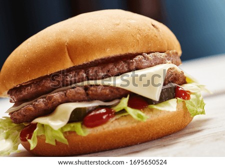 Close-up of delicious fresh home made burger with lettuce, cheese, onion and tomato on a rustic wooden plank on a dark background.