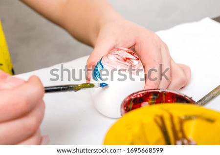 Girl paints and brushes paints a white egg for Easter