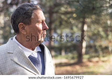 Portrait of a pensive senior man sitting on the bench, in the public park, outdoors. Old man relaxing outdoors and looking away. Portrait of senior man looking thoughtful