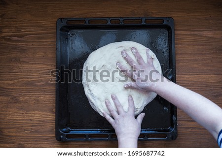Picture of a person stretching a pizza dough on a baking tray from the oven, top view