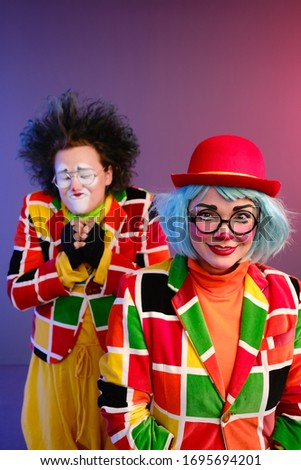 Two clowns a man and a woman with makeup in bright colored costumes are fooling around and showing a presentation using various accessories. April Fools Day concept. Birthday for kids