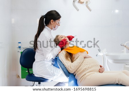 A professional dentist treats and examines the oral cavity of a pregnant girl in a modern dental office. Dentistry Royalty-Free Stock Photo #1695698815