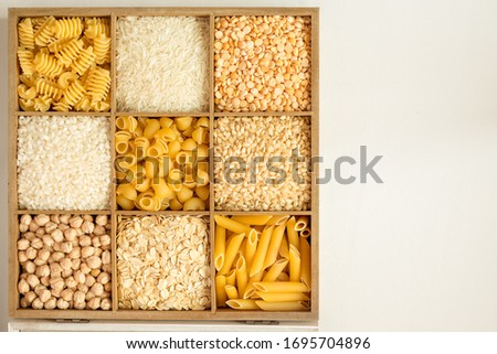 wood box with different typs of non-perishable food (pasta,rice, cereals, cheakpeas) at the white table Royalty-Free Stock Photo #1695704896