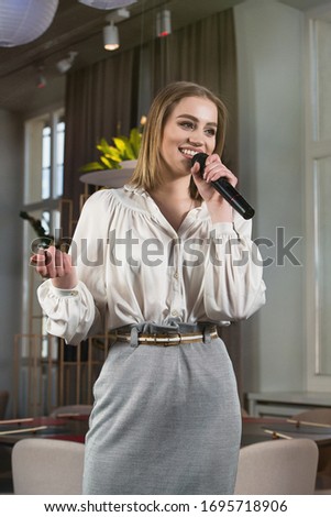 Business and speech topic: woman in a white blouse holding a black microphone, indoor