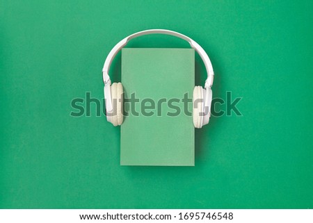 Book is white with headphones on green background. Top view.