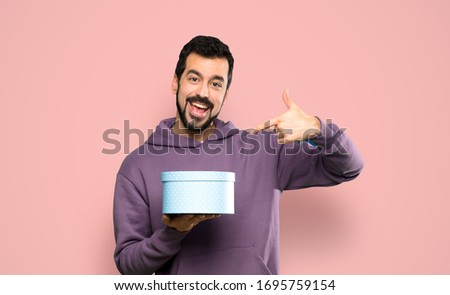 Handsome man with sweatshirt holding a gift over isolated pink background