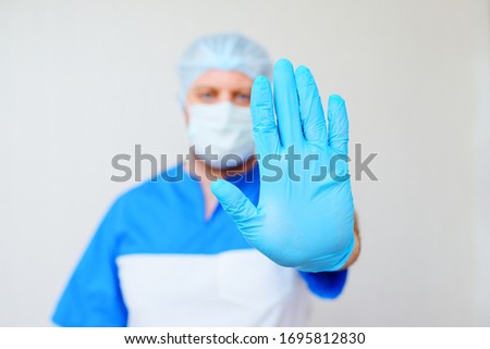 doctor man showing a stop gesture with your hand wearing rubber gloves on a light background. Stopping the disease, coronavirus, covid19