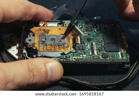The master is repairing a broken camera. Repair the old camera. A screwdriver unscrews the nut.