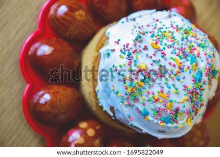 Close up picture of Easter cake with eggs on the side with traditional name kulich with sprinkling of small dots in different colors in orthodox church with painted eggs as decoration process.