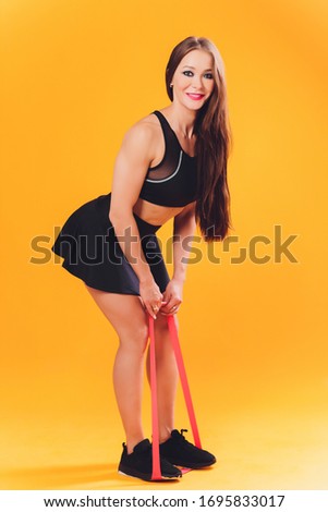 Athletic girl performs exercises using a resistance band. Photo of young girl on background. Strength and motivation.