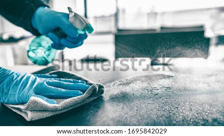 Cleaning home table sanitizing kitchen table surface with disinfectant spray bottle washing surfaces with towel and gloves. COVID-19 prevention sanitizing inside. Royalty-Free Stock Photo #1695842029