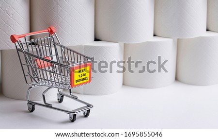 shopping cart model with message KEEP 1.5M DISTANCE in front of stockpile of toilet paper