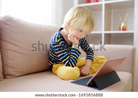 Preschooler boy is watching movies or cartoon movie from tablet sitting on couch. Entertainments for little kids while coronavirus pandemic. Stay at home during quarantine.