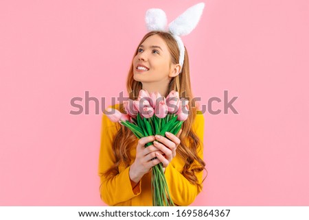 happy Easter. Happy pensive woman in the ears of an Easter Bunny, a girl with a bouquet of tulips, on an isolated pink background