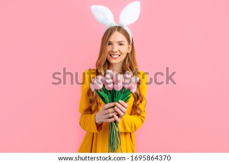 happy Easter. Happy attractive woman in Easter Bunny ears, girl with a bouquet of tulips, on an isolated pink background