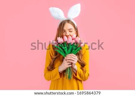 happy Easter. Happy attractive woman in Easter Bunny ears, girl with a bouquet of tulips, on an isolated pink background
