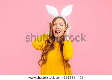 happy Easter. Happy stylish woman in Easter Bunny ears, covers her ears with her hands, on an isolated pink background