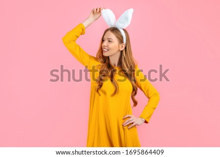 Holiday season of rabbit and eggs. A happy stylish woman in Easter Bunny ears isolated on a pink background looks at the space.