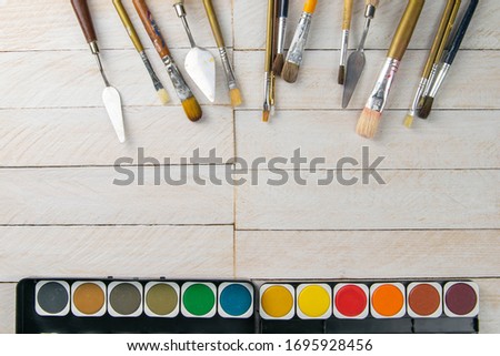 Set of artist accessories collection. Canvas, tube of oil paint, art brushes, palette knife lying on the wood table. Artist workshop background.