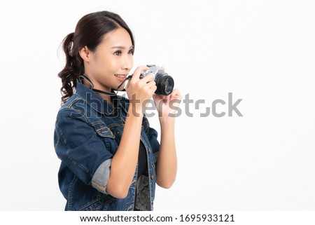 Beautiful female tourist wearing a black hat and jeans jacket is standing to take a picture with a vintage camera in happiness at studio shot isolated on white background.