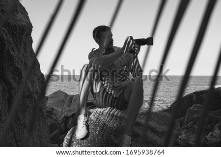 A man with a camera in his hand sits on the rocks by the sea in on a summer day