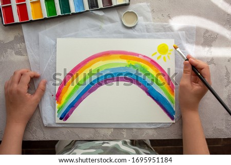 Young boy painted rainbow with color during pandemic coronavirus quarantine. Child painting rainbows around the world with the words Let's all be well.