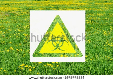 Yellow biological hazard warning sign on the backdrop of green field with dandelions, spring, copy space.