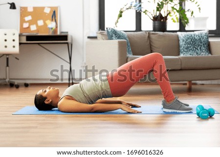 sport, fitness and healthy lifestyle concept - african american woman doing pelvic lift abdominal exercise at home Royalty-Free Stock Photo #1696016326